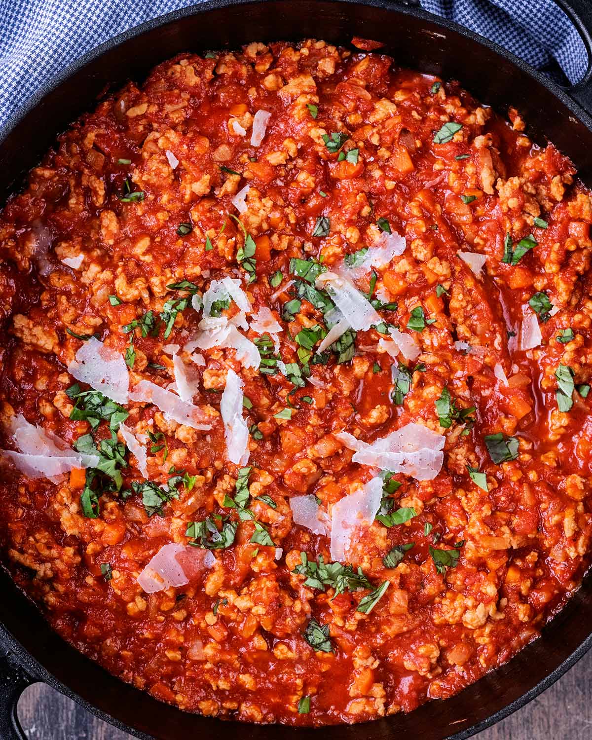 Cooked bolognese with chopped basil and Parmesan shavings on top.