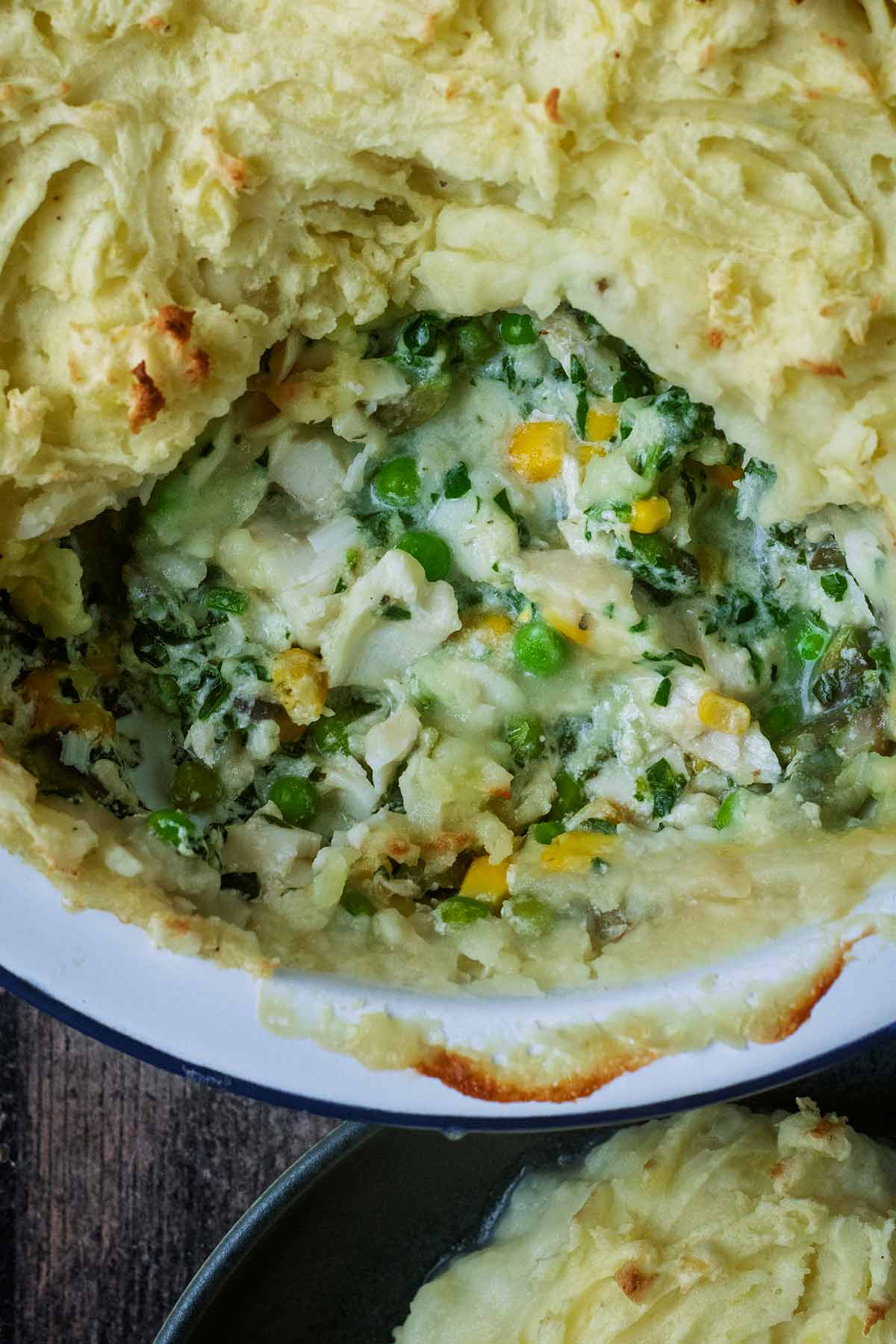 Fish pie with a portion removed showing the insides of fish and vegetables in a creamy sauce.