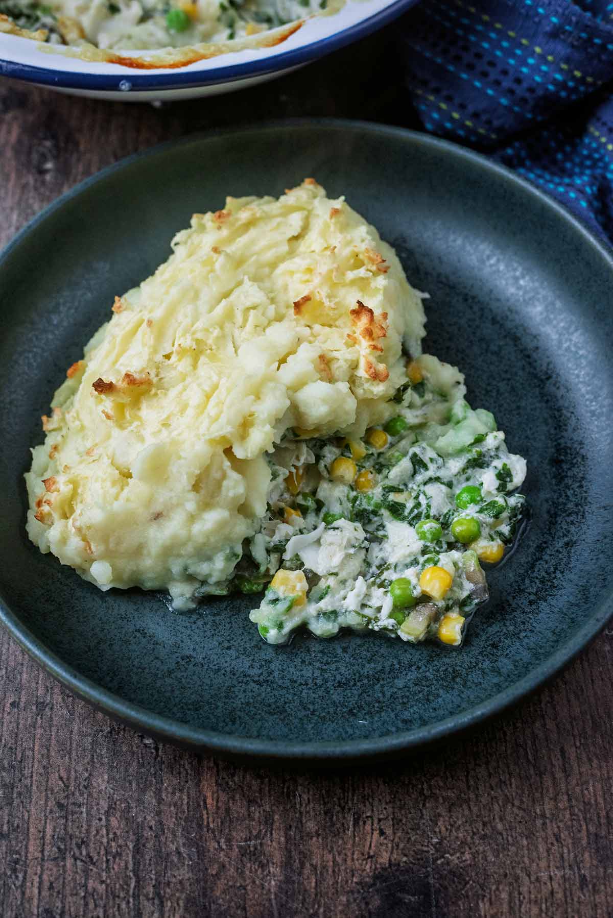 A portion of potato topped fish pie in a dark blue bowl.