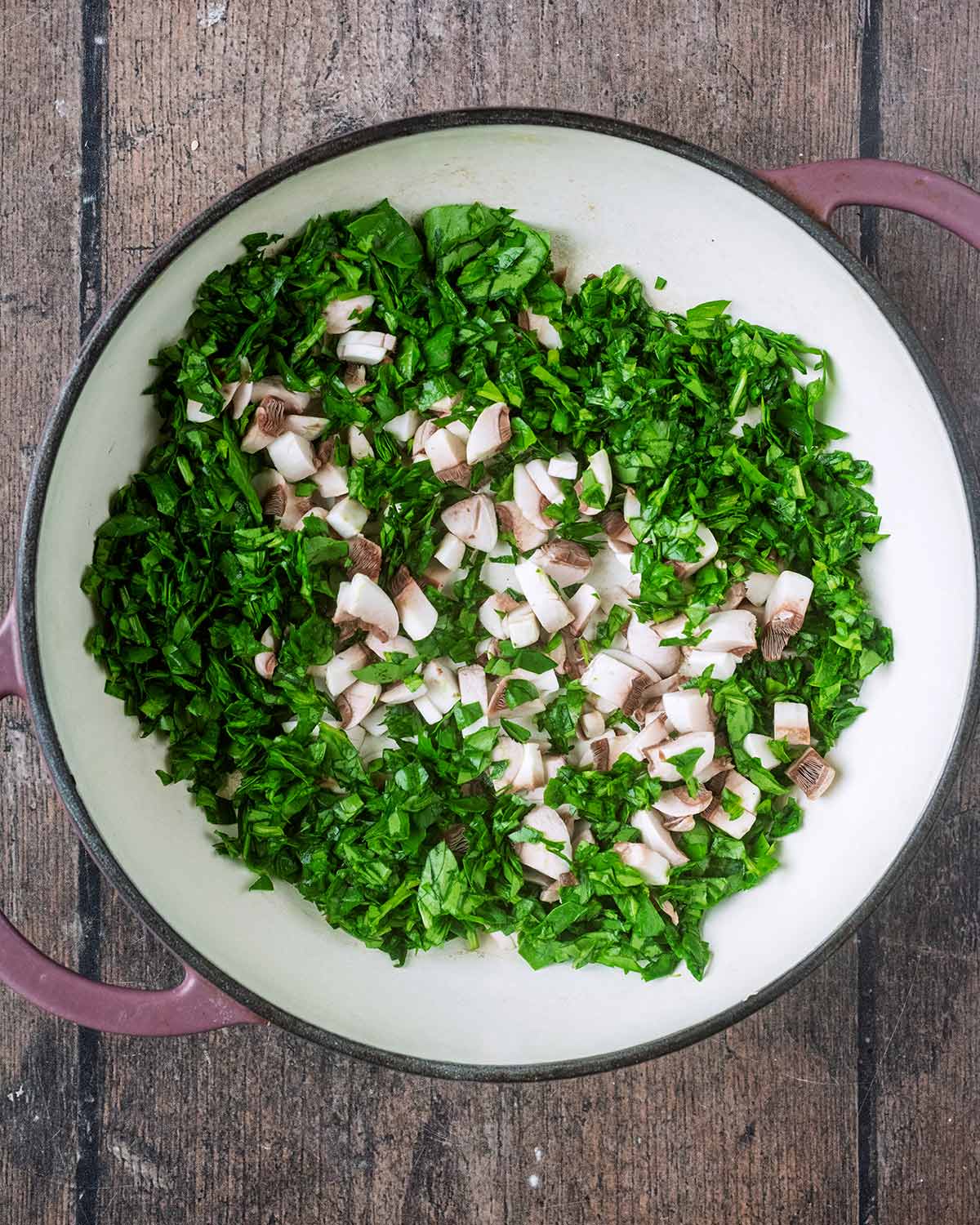 A large pan with chopped mushrooms and chopped spinach in it.