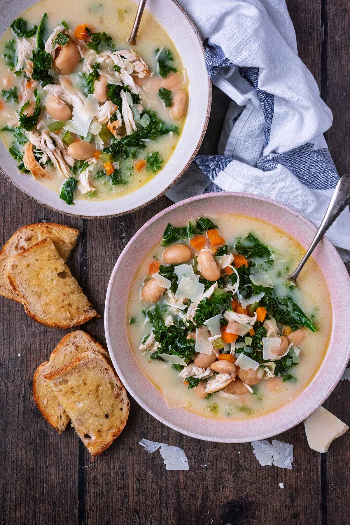 Two bowls of chicken and bean soup next to slices of buttered toast.