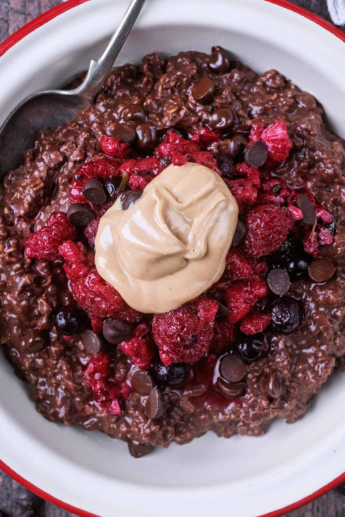 A bowl of chocolate porridge topped with frozen berries and a dollop of nut butter.