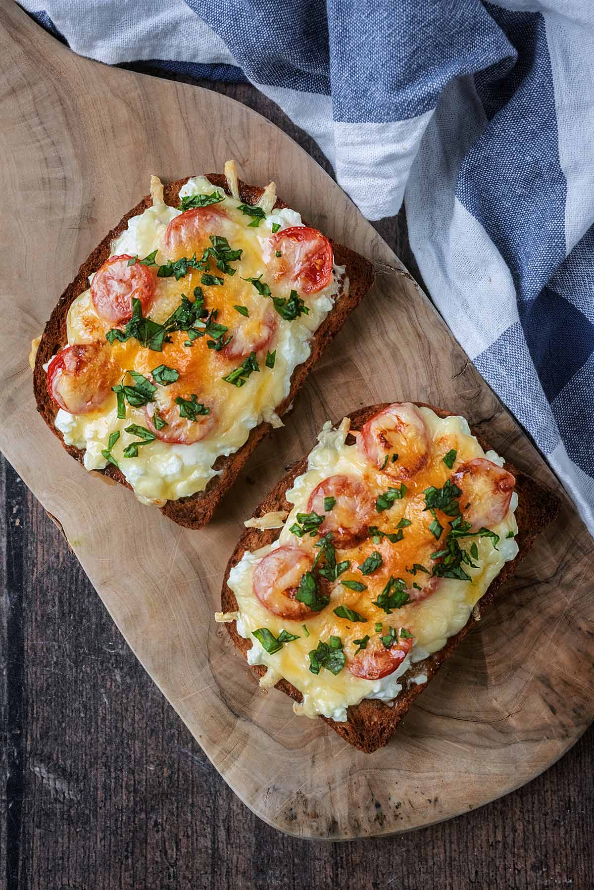 Two slices of cheese and tomatoes on toast on a wooden serving board.