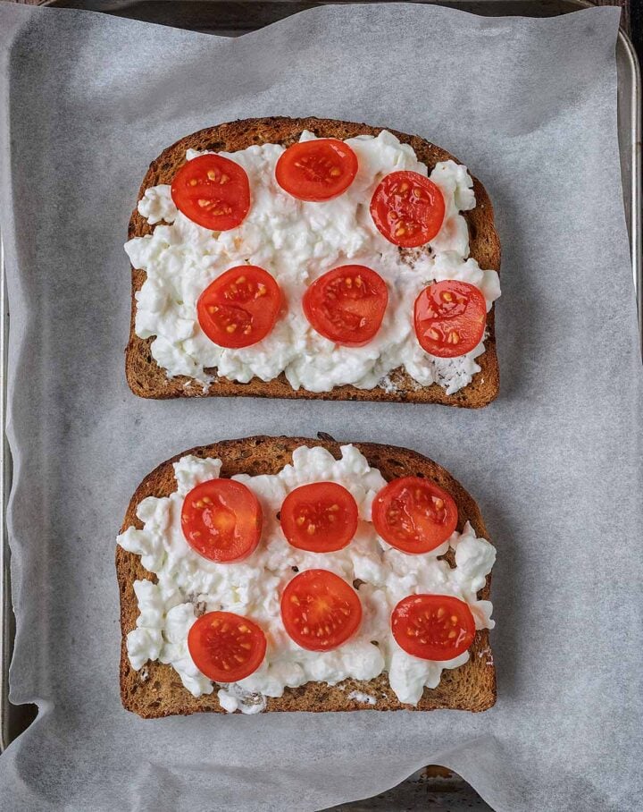 Two slices of toast topped with cottage cheese and sliced cherry tomatoes.