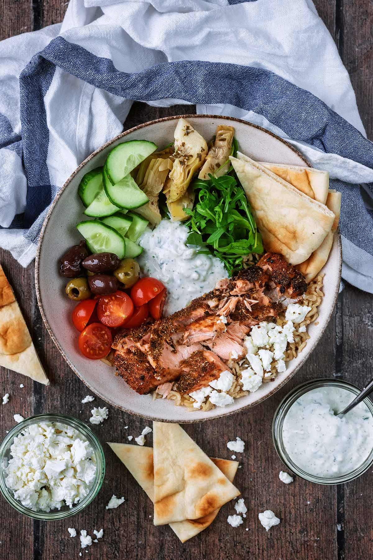 A bowl of rice, salad vegetables, tzatziki and a flaked salmon fillet.