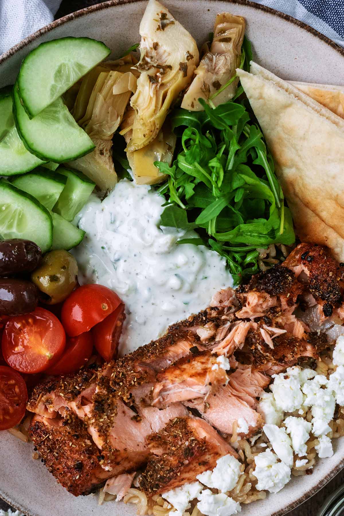 Cooked salmon, tomatoes, cucumber, lettuce, olives, artichokes and lettuce in a serving bowl.