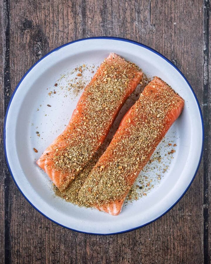 Two uncooked seasoned salmon fillets on a plate.