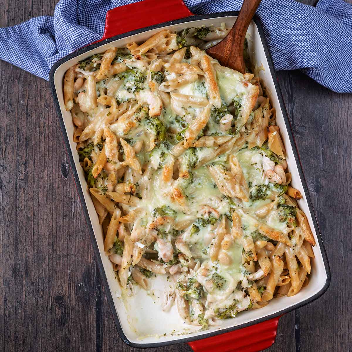 A tray of chicken and broccoli pasta bake with a portion removes.
