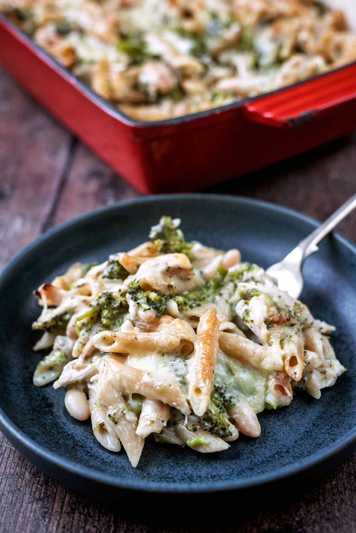 A plate of pasta bake in front of a tray of more pasta bake.
