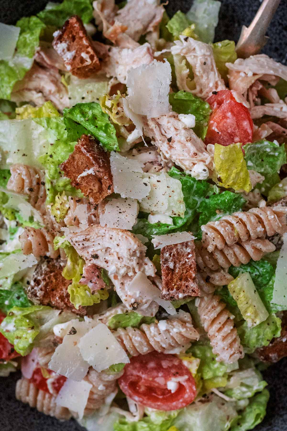 Parmesan shavings on top of a chicken pasta salad.