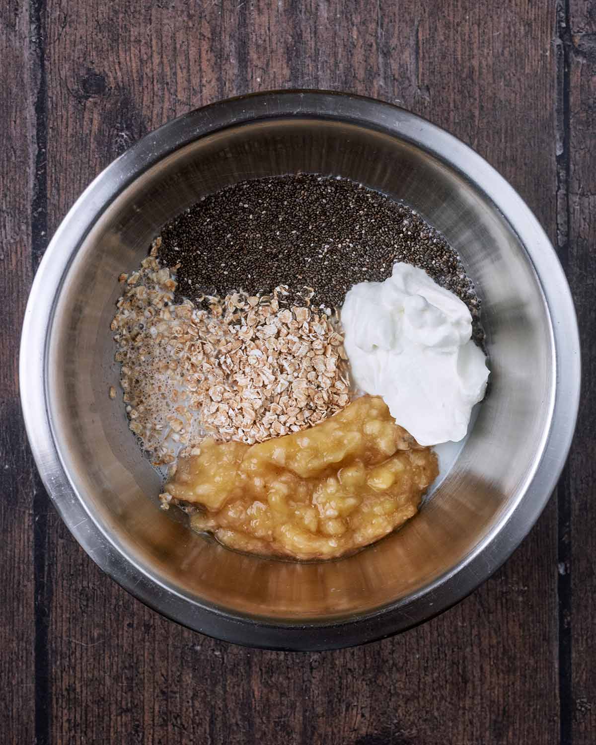 Oats, chia seeds, yogurt and mashed banana in a mixing bowl.