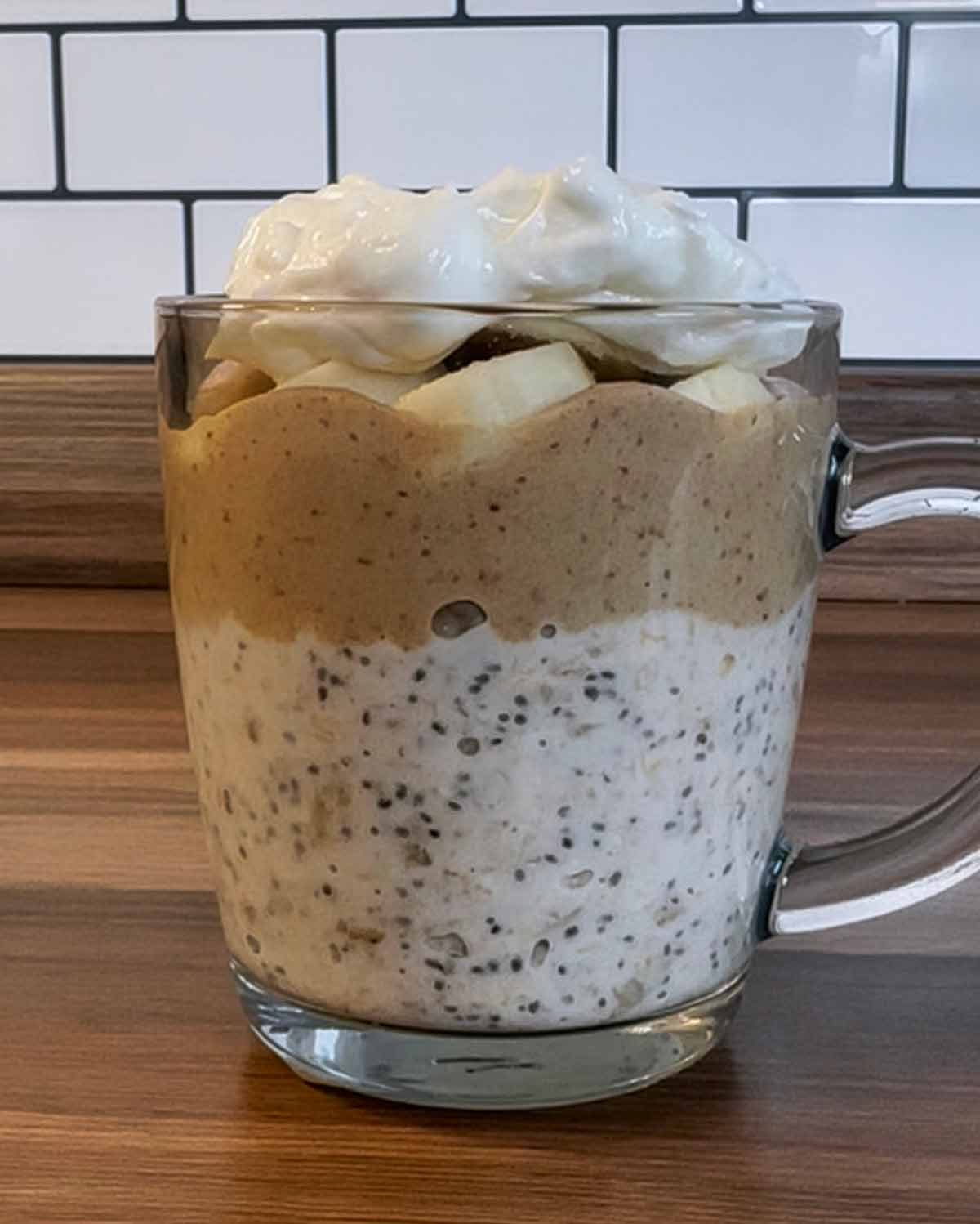A glas mug layered with oats, caramel, banana and yogurt.