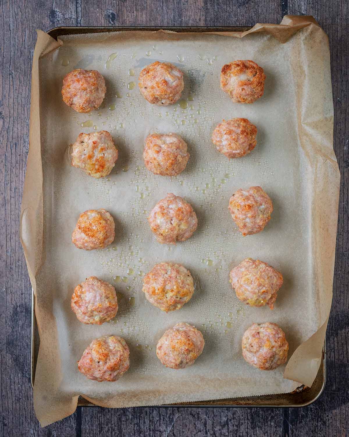 Fifteen cooked meatballs on a baking sheet.