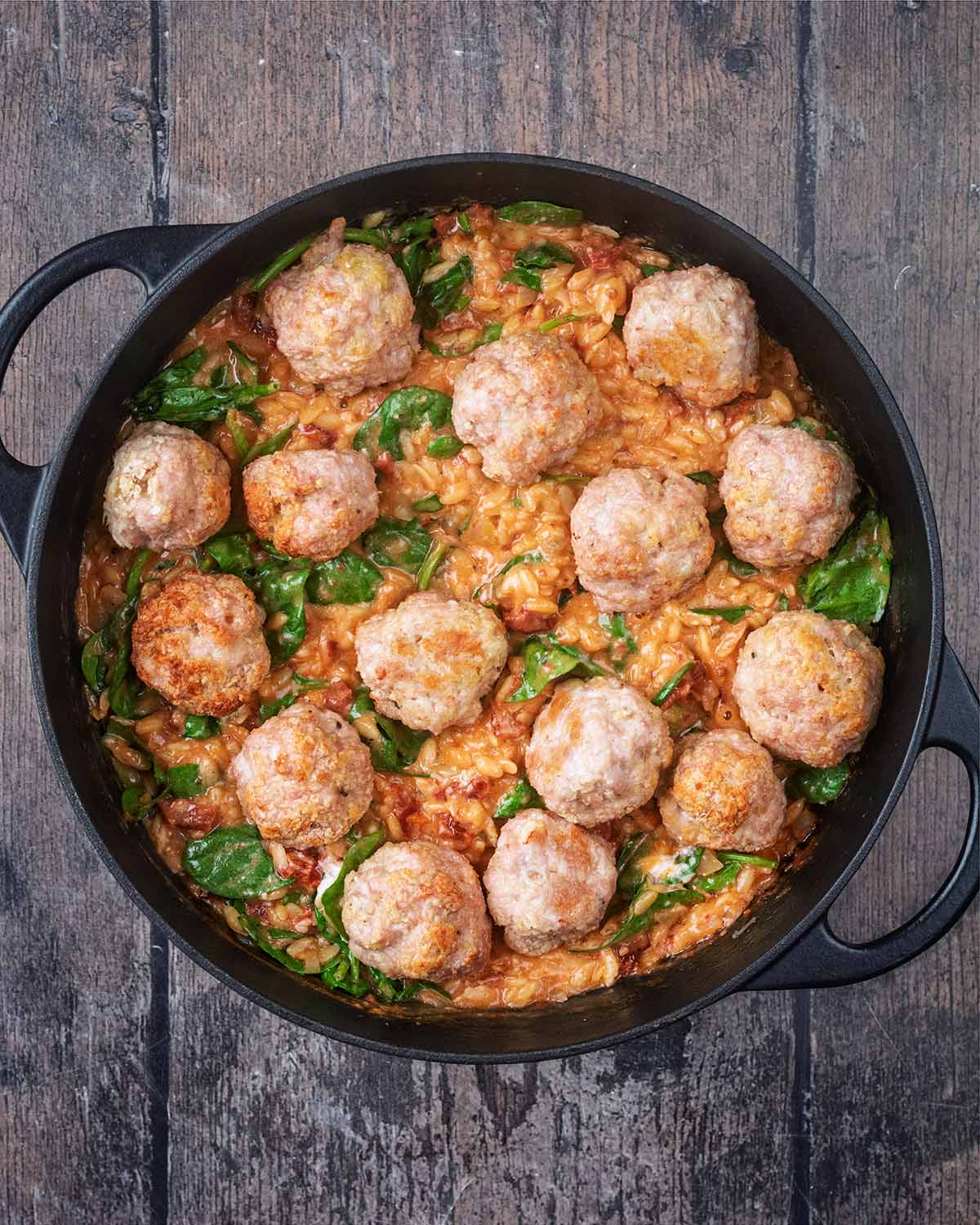 Cooked meatballs added to the orzo sauce in the pan.