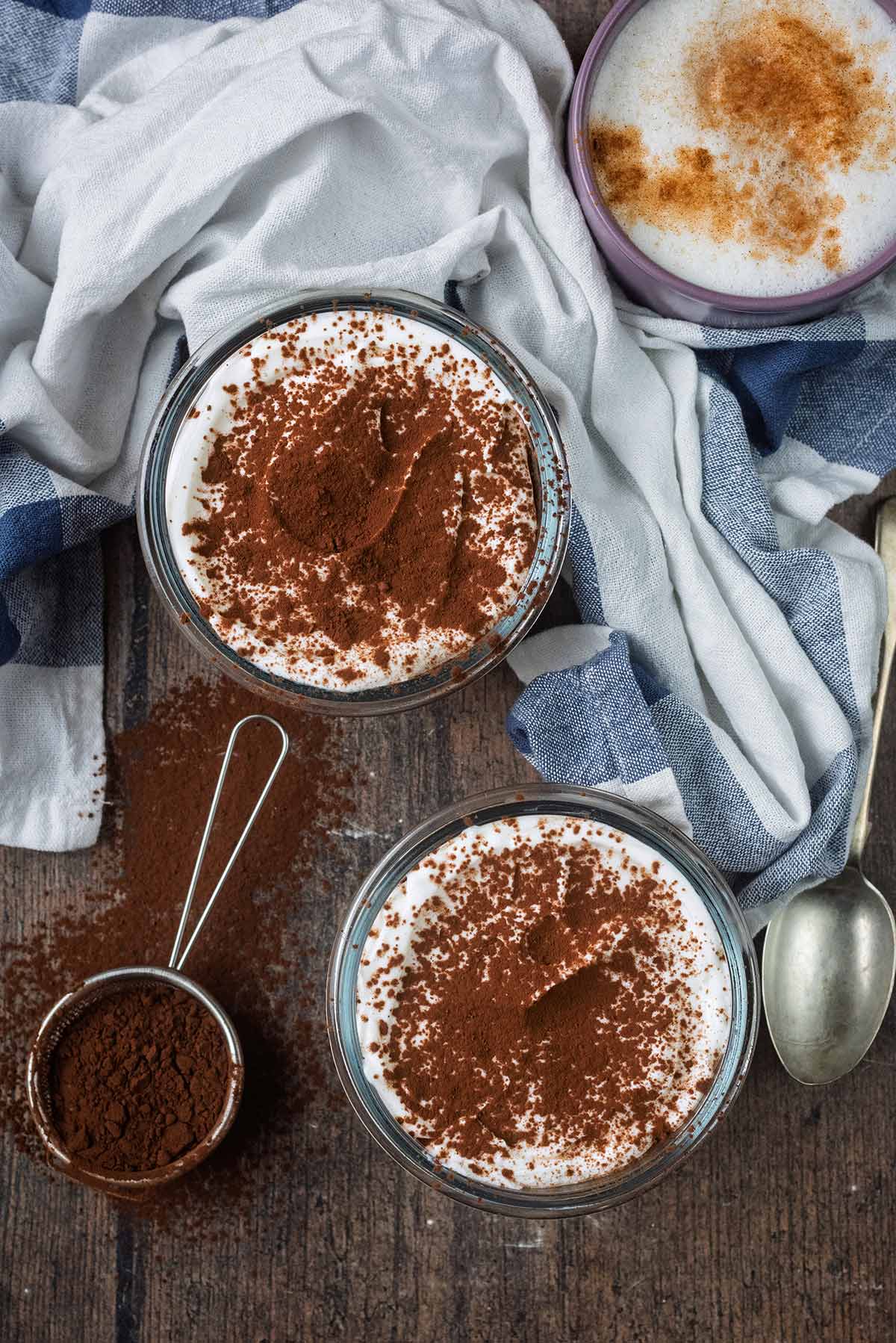 Two pots of cocoa topped overnight oats next to a cup of coffee and a striped towel.