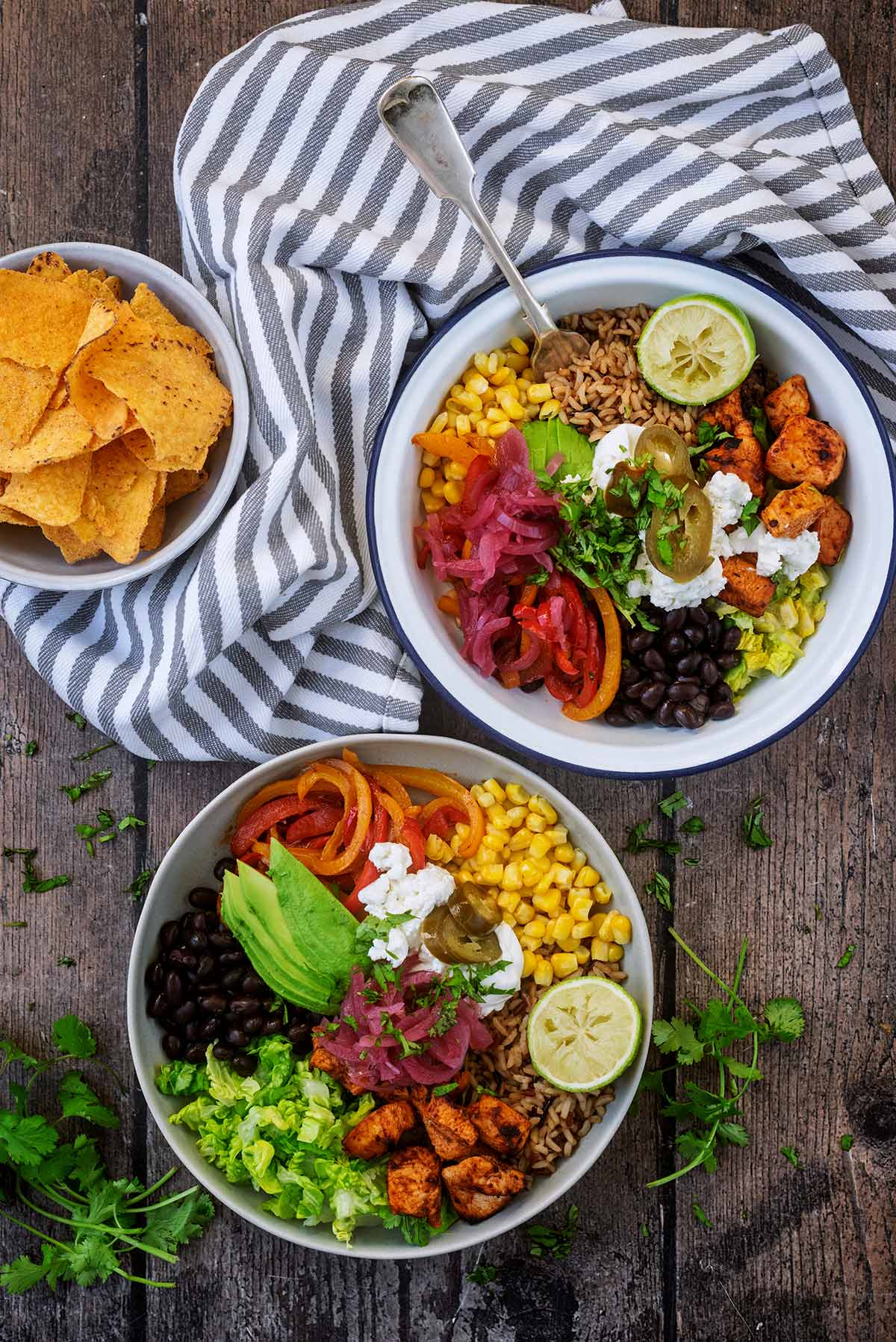 Two chicken fajita bowls next to a bowl of tortilla chips and a striped towel.