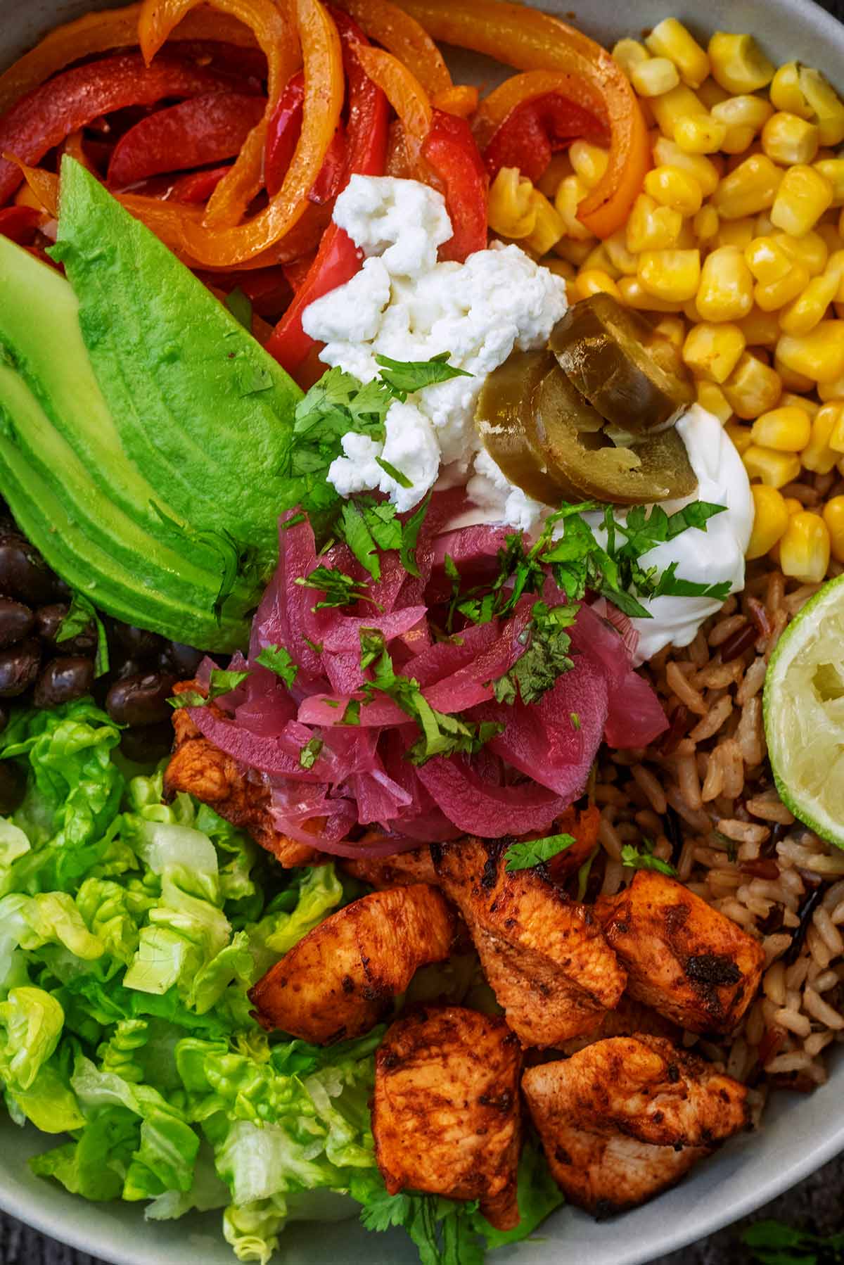 Cooked chicken chunks, chopped lettuce, sliced avocado, sweetcorn, red onions and yogurt arranged in a bowl.