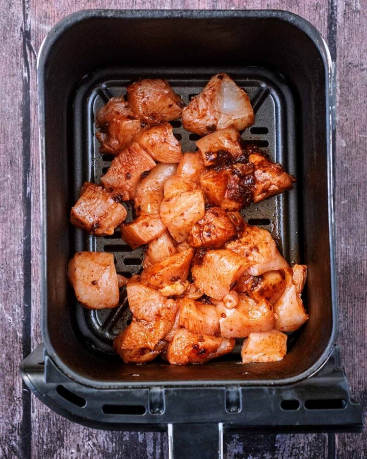 Coated chicken chunks in an air fryer basket.