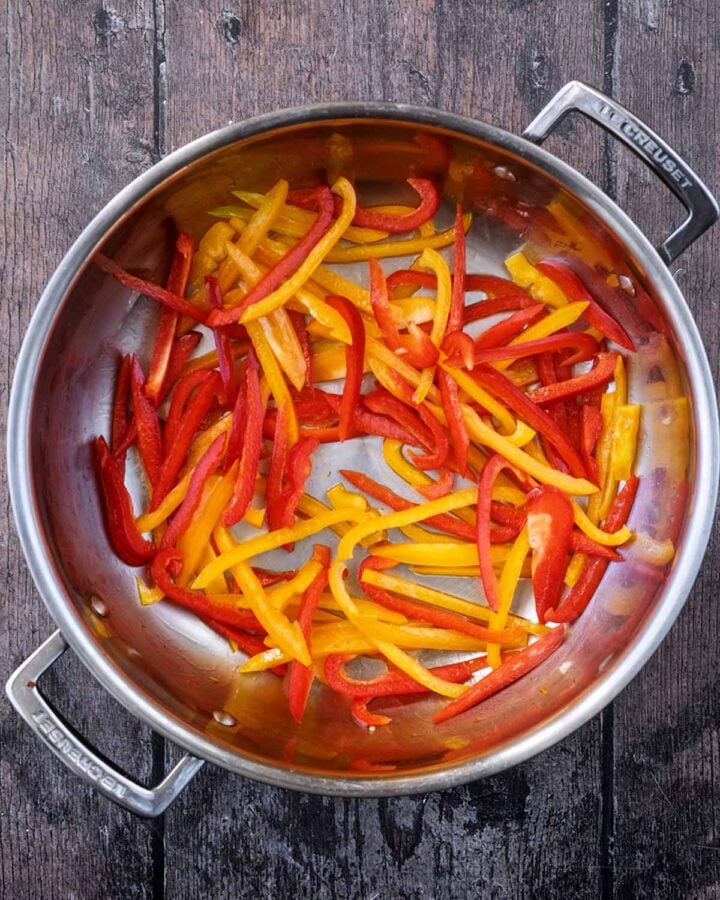 Sliced bell peppers cooking in a large pan.