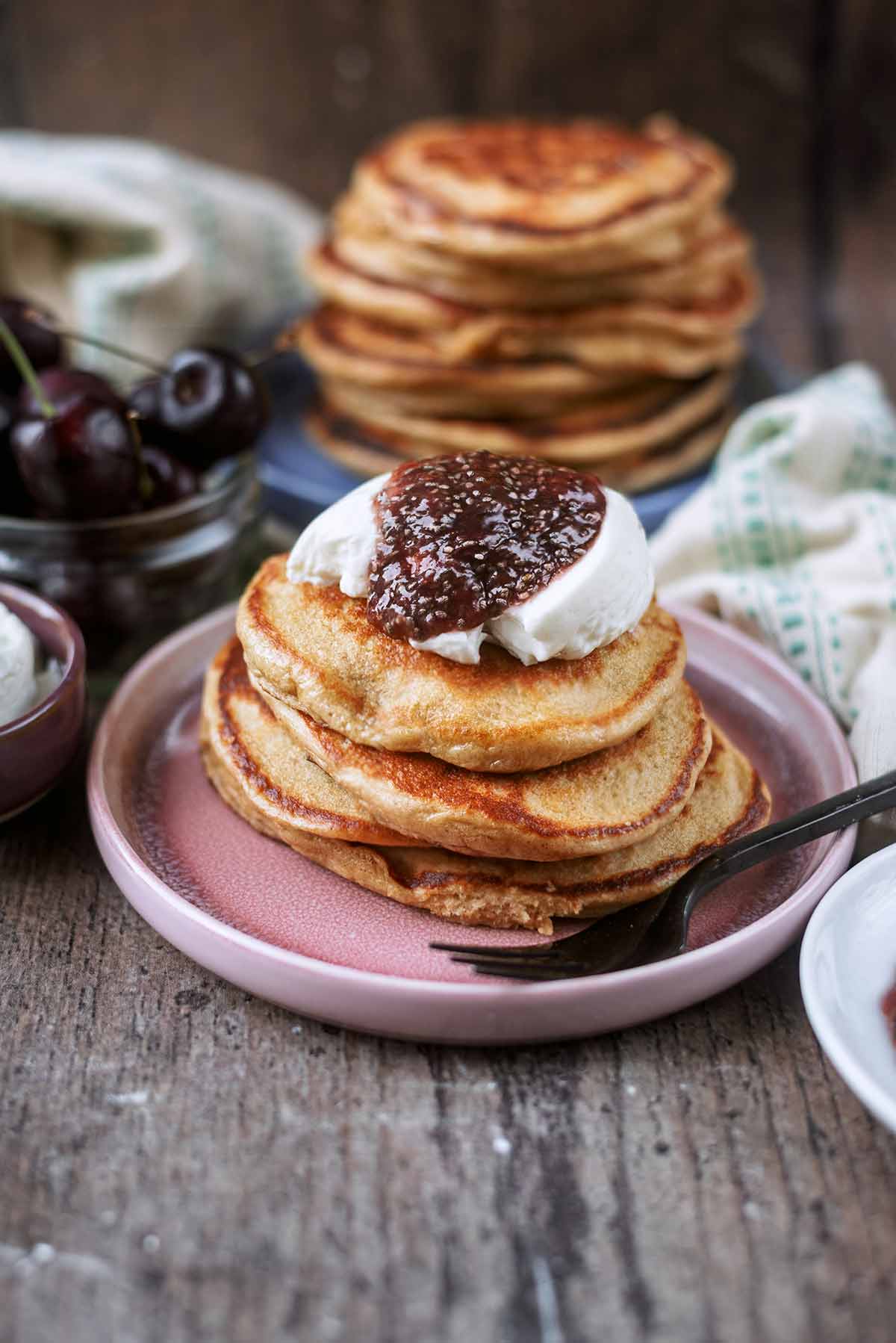 A stack of pancakes on a pink plate with another stack in the background.