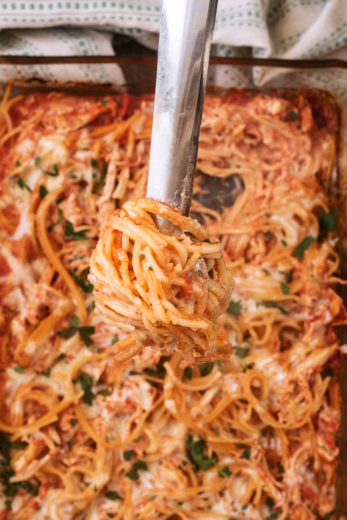A pair of tongs with tomato spaghetti twisted around them.