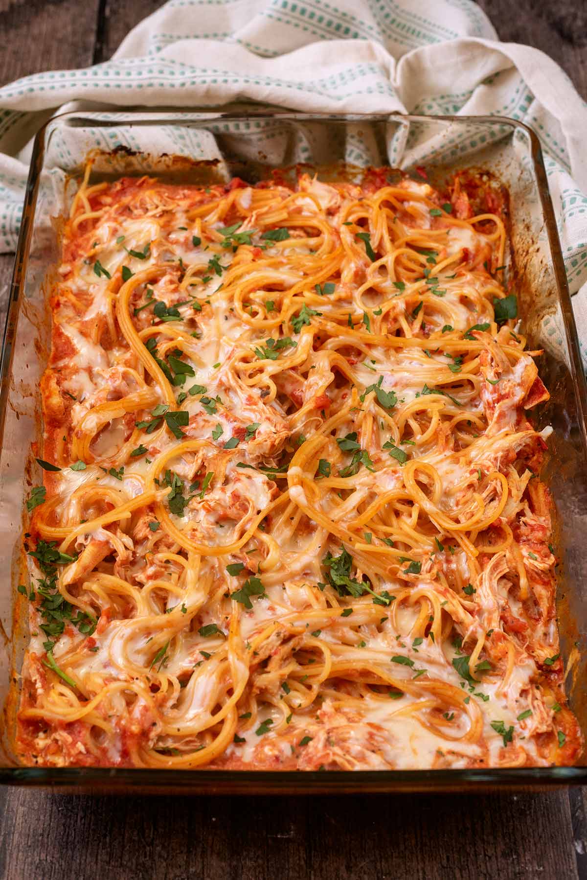A baking dish full of spaghetti bake in front of a patterned towel.