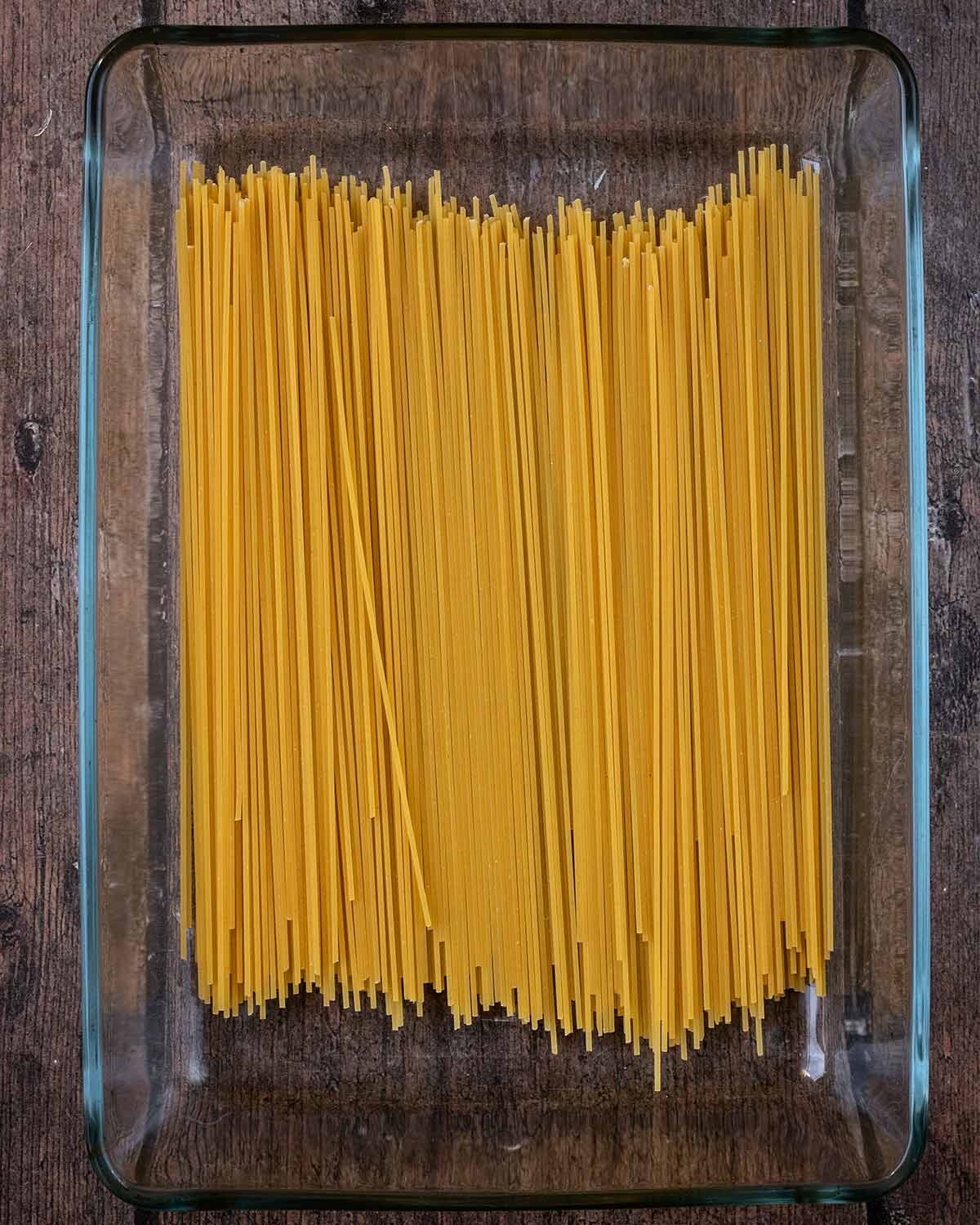 Strands of dry spaghetti in a large glass baking dish.