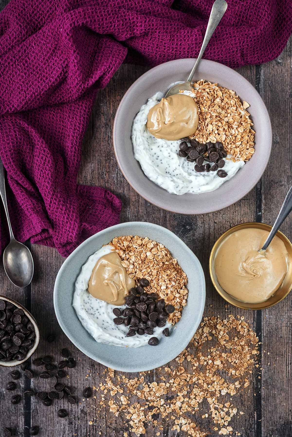 Two bowls of chia yogurt topped with oats, nut butter and chocolate chips.