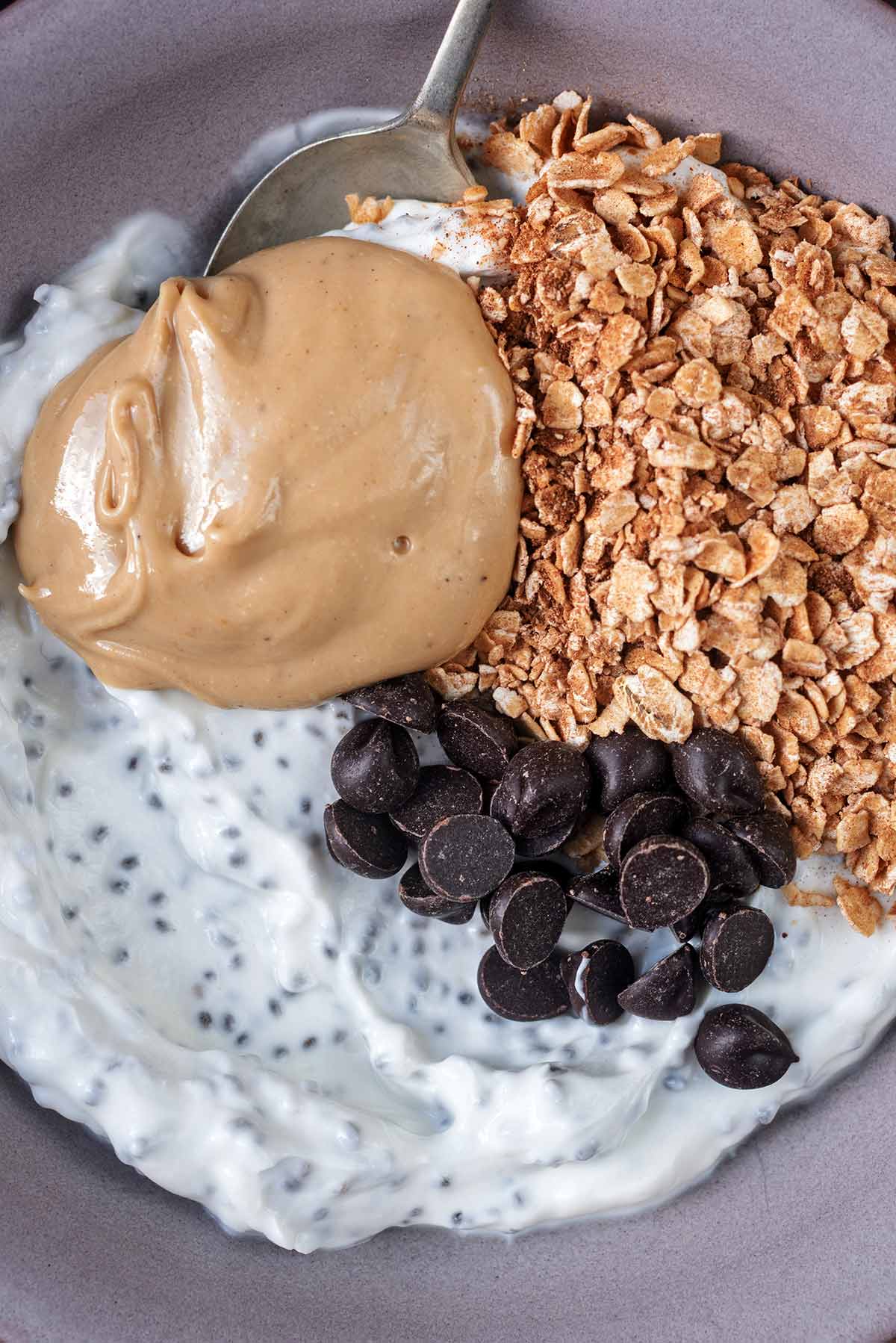 Chia yogurt, a dollop of nut butter, oats and chocolate chips, with a spoon.