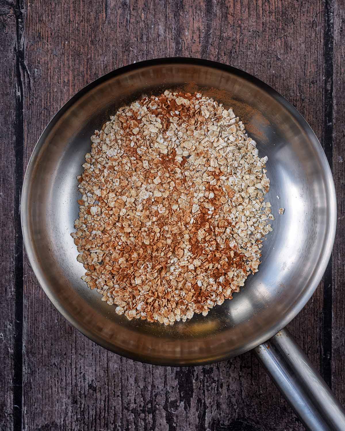 Oats and ground cinnamon in a small silver frying pan.