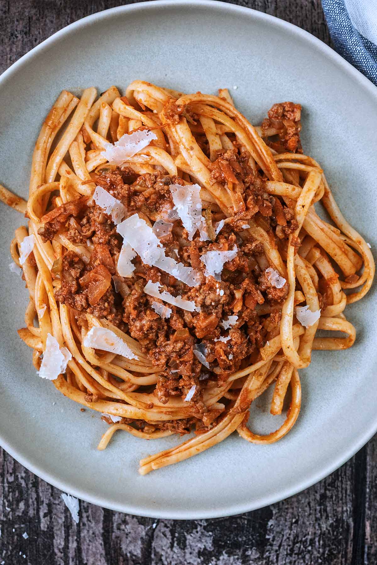 A plate of pasta bolognese topped with Parmesan shavings.