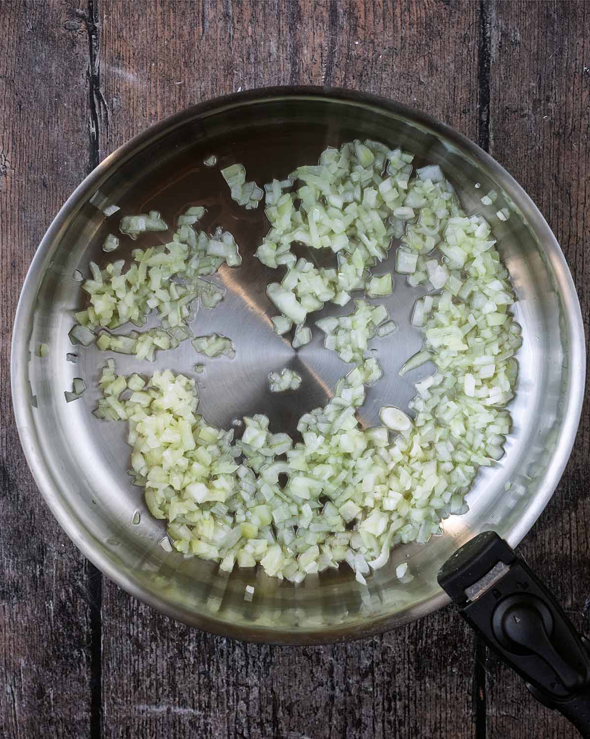 Diced onions cooking in a large silver pan.