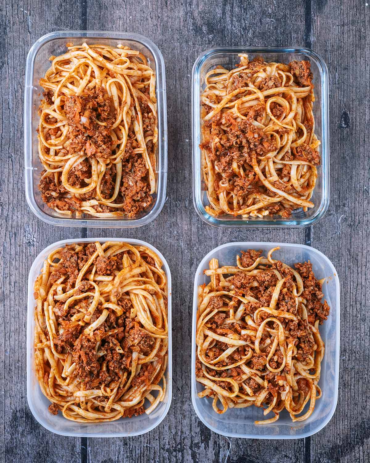Four storage containers with pasta bolognese in them.