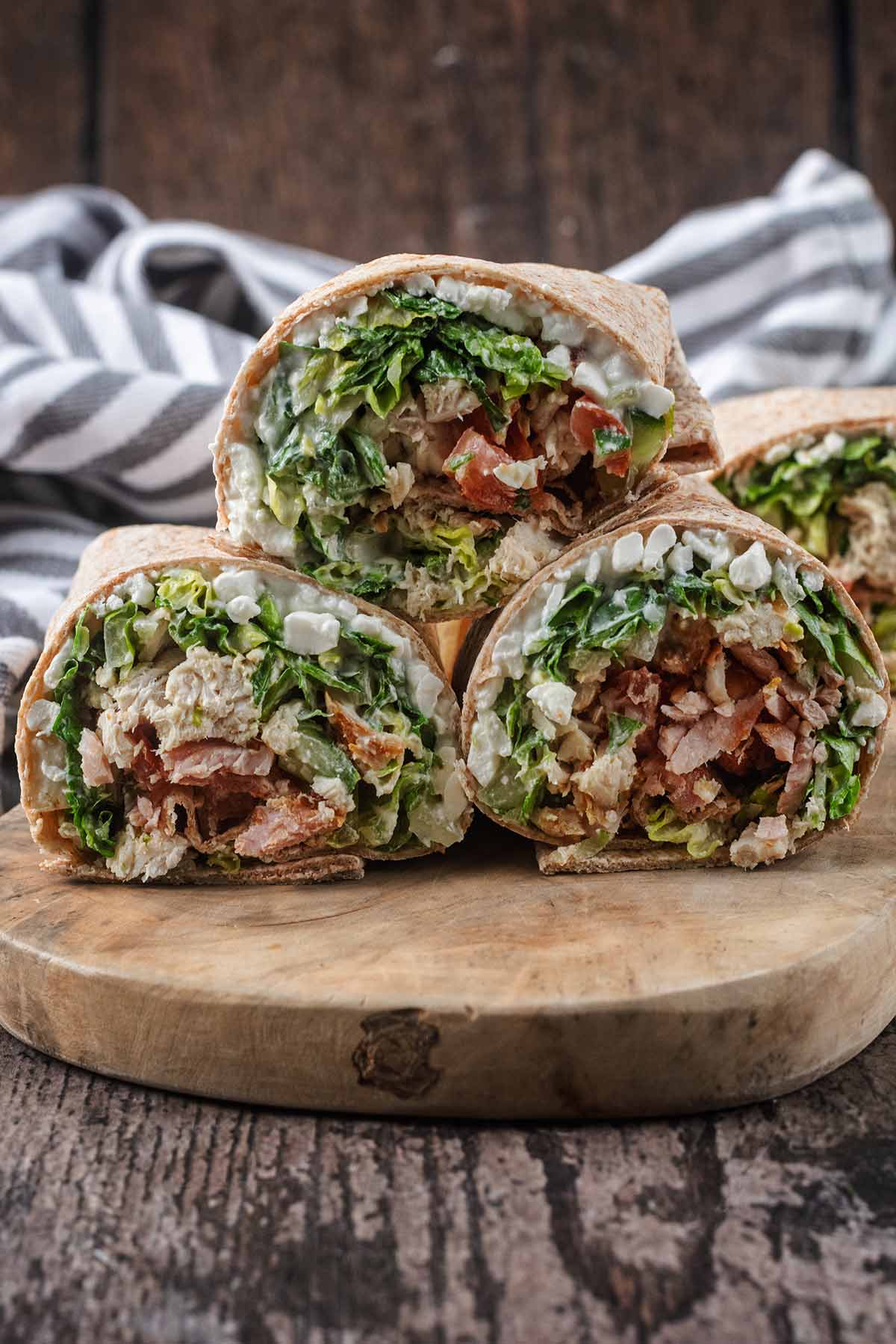 Three chicken salad wraps sat on a wooden serving board.