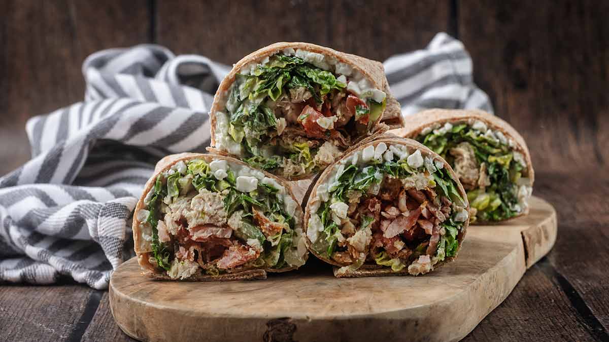 Three high protein chicken Caesar wraps on a wooden board.