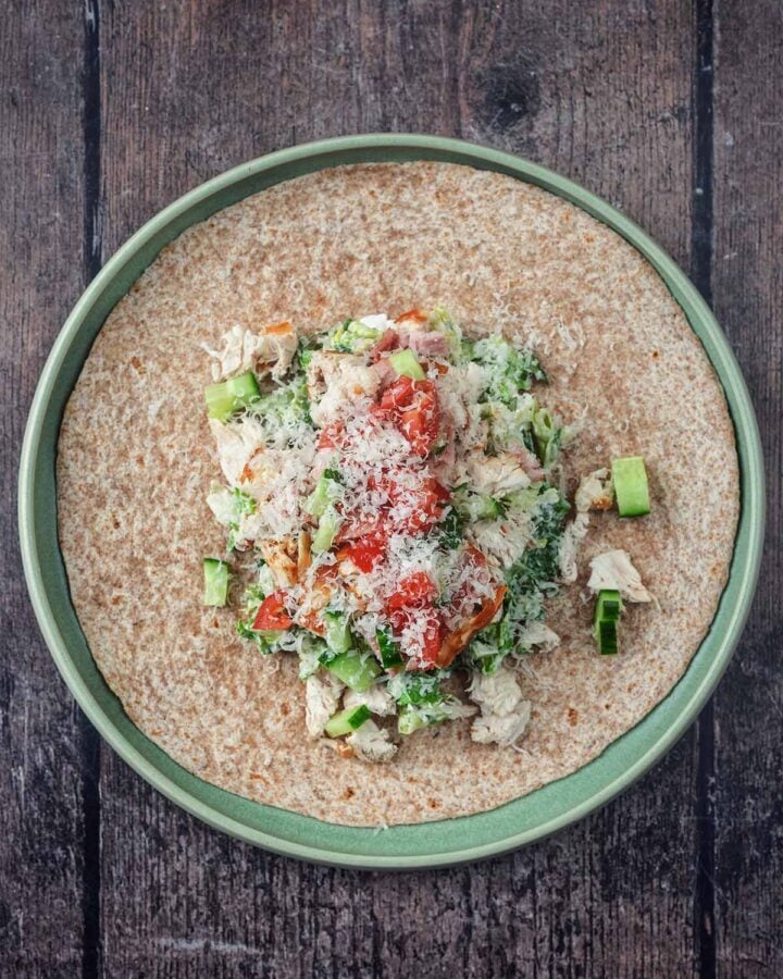 A large wrap with dressed lettuce, chopped chicken, chopped bacon, salad veg and grated cheese.