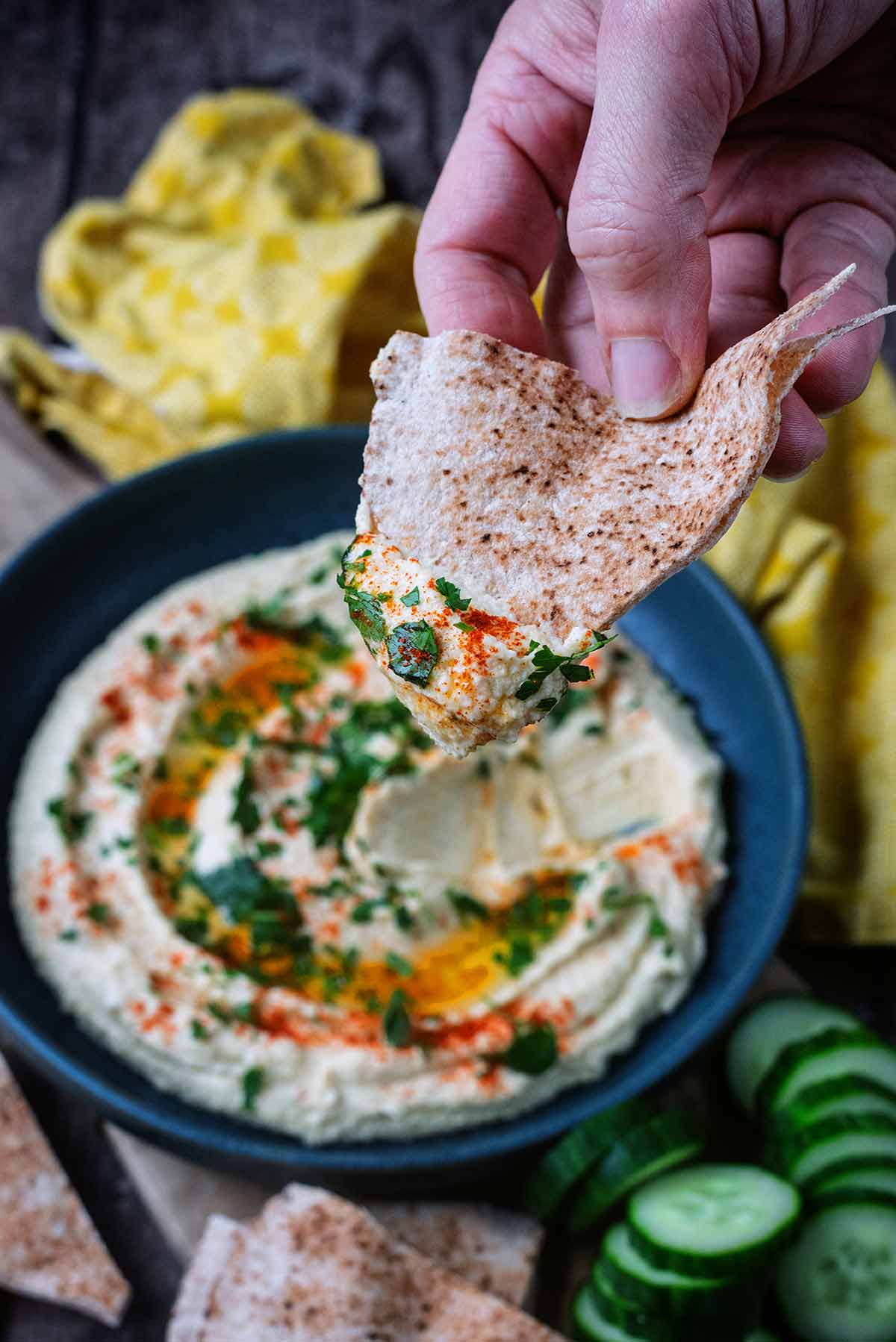 A hand holding a flatbread that has been dipped into some hummus.