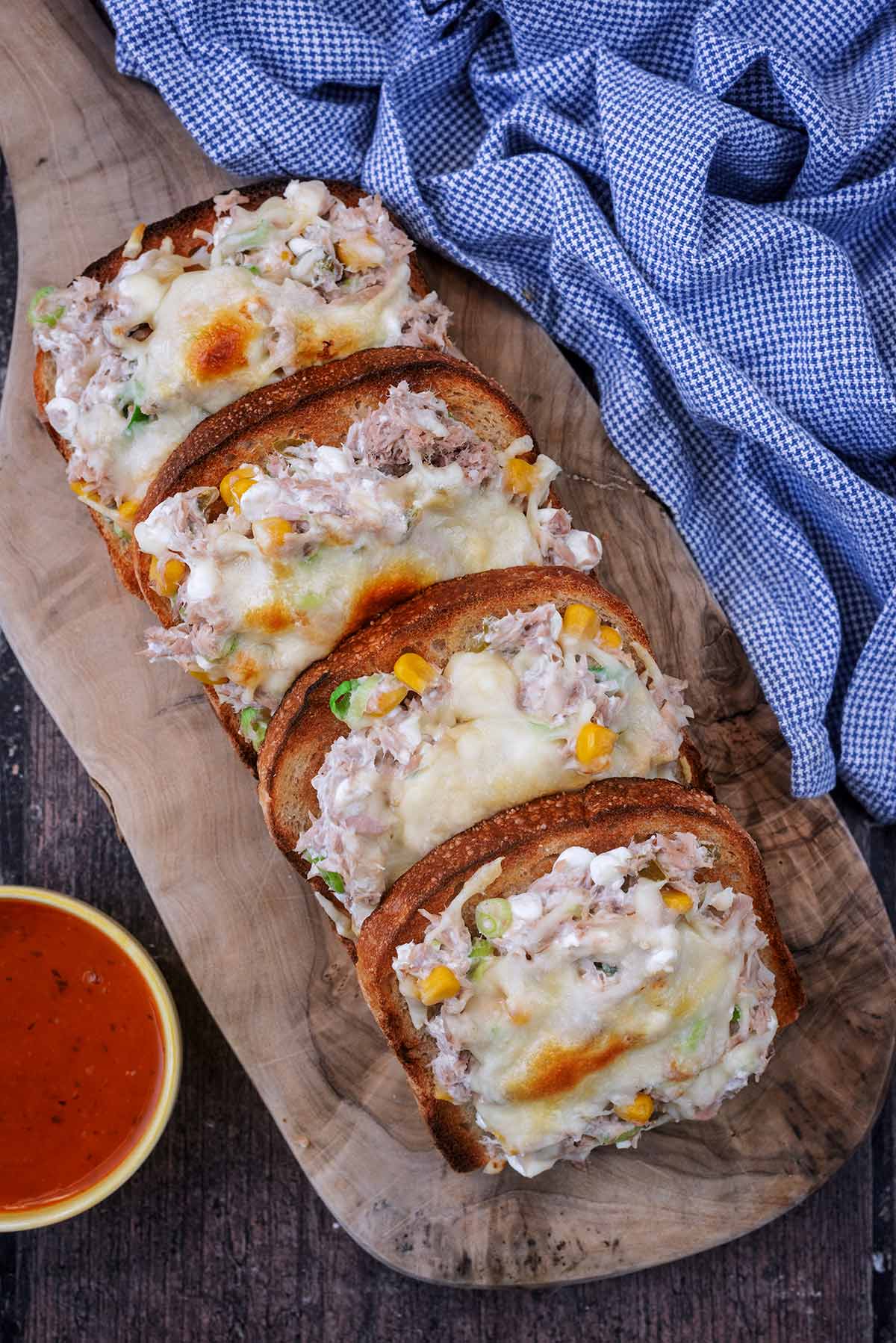 Four slices of tuna melt on a wooden serving board.