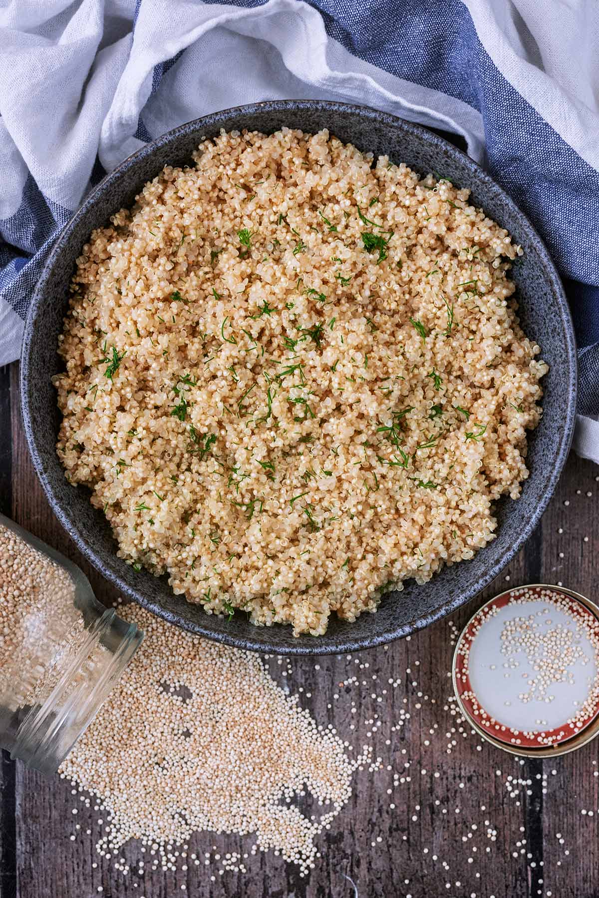 A bowl of cooked quinoa with a jar of uncooked quinoa spilled out in front of the bowl.