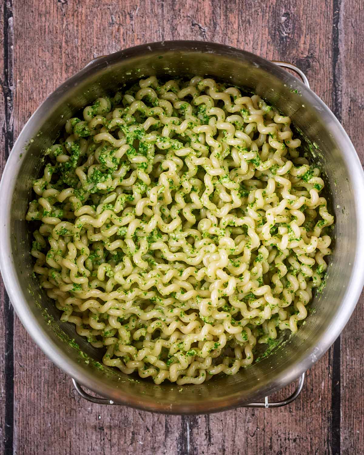 A pan of cooked pasta with pesto mixed into it.