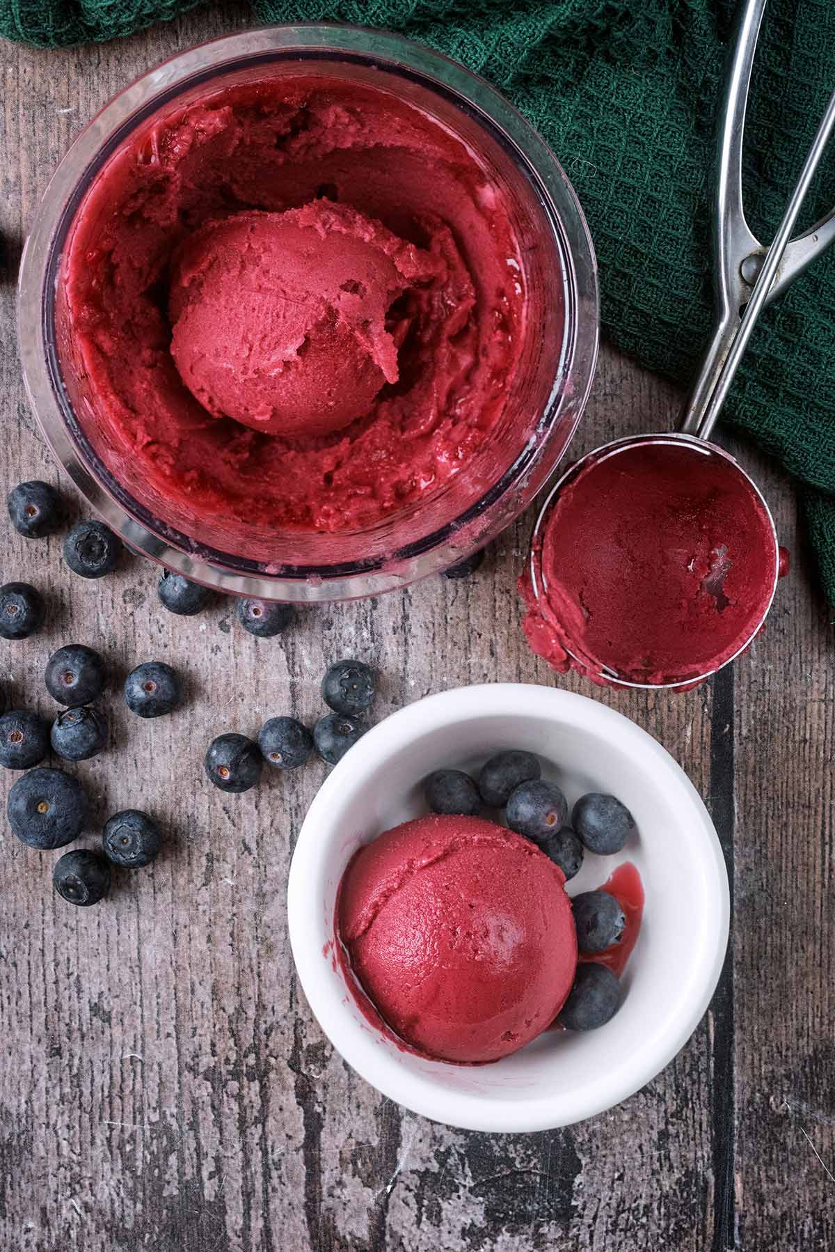 A ball of red sorbet in a bowl next to a Ninja Creami tub containing more sorbet.