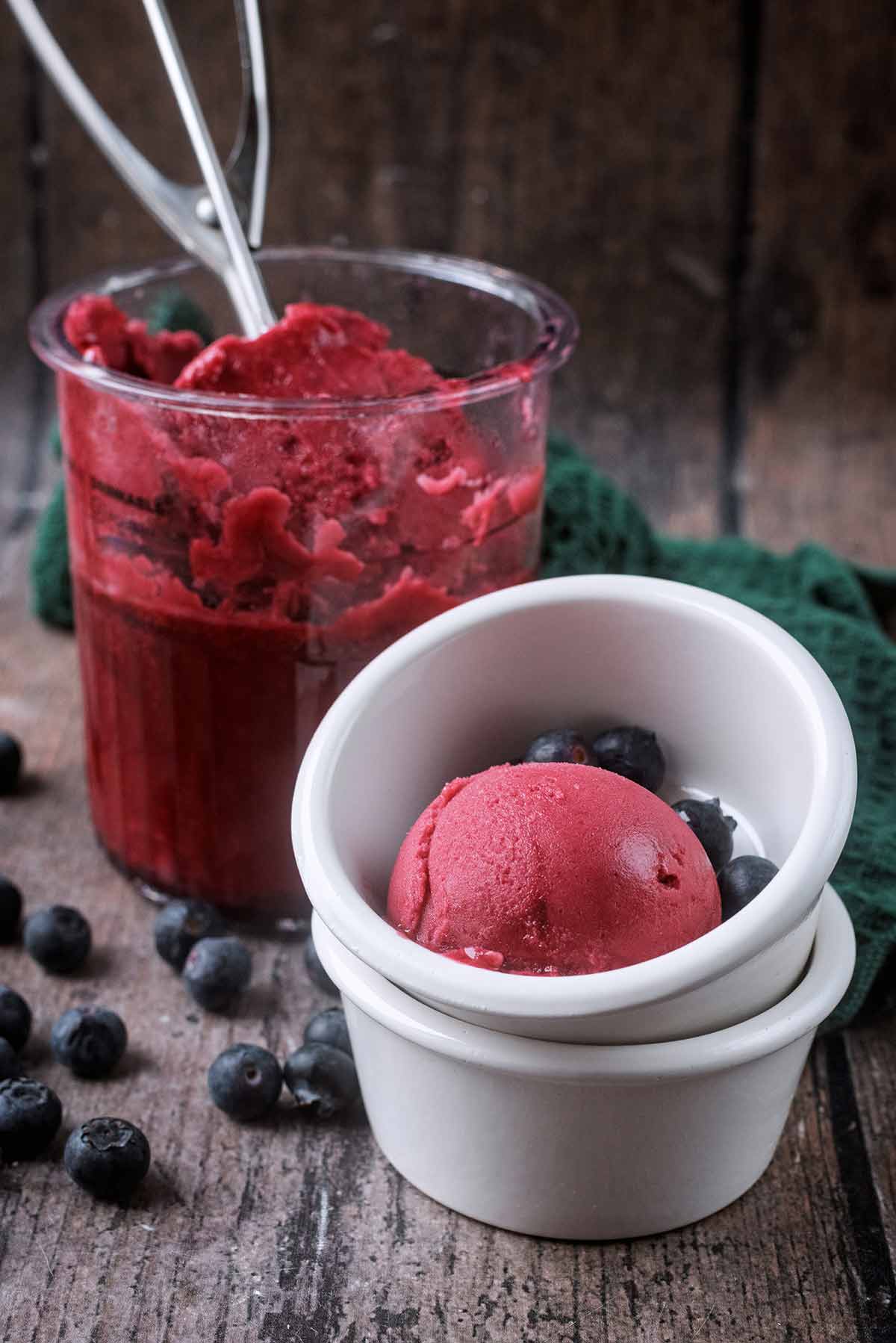 A bowl of berry sorbet in front of a Ninja Creami pint tub with an ice cream scoop in it.