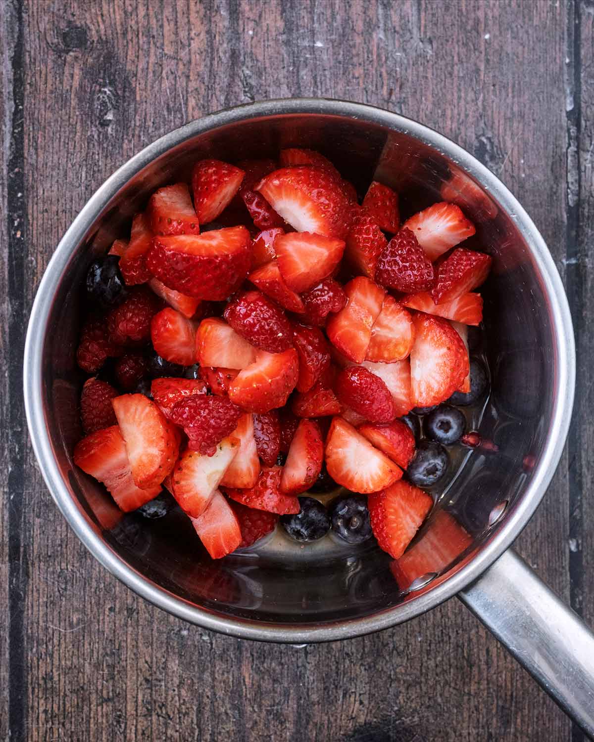 A saucepan containing blueberries, raspberries and chopped strawberries.