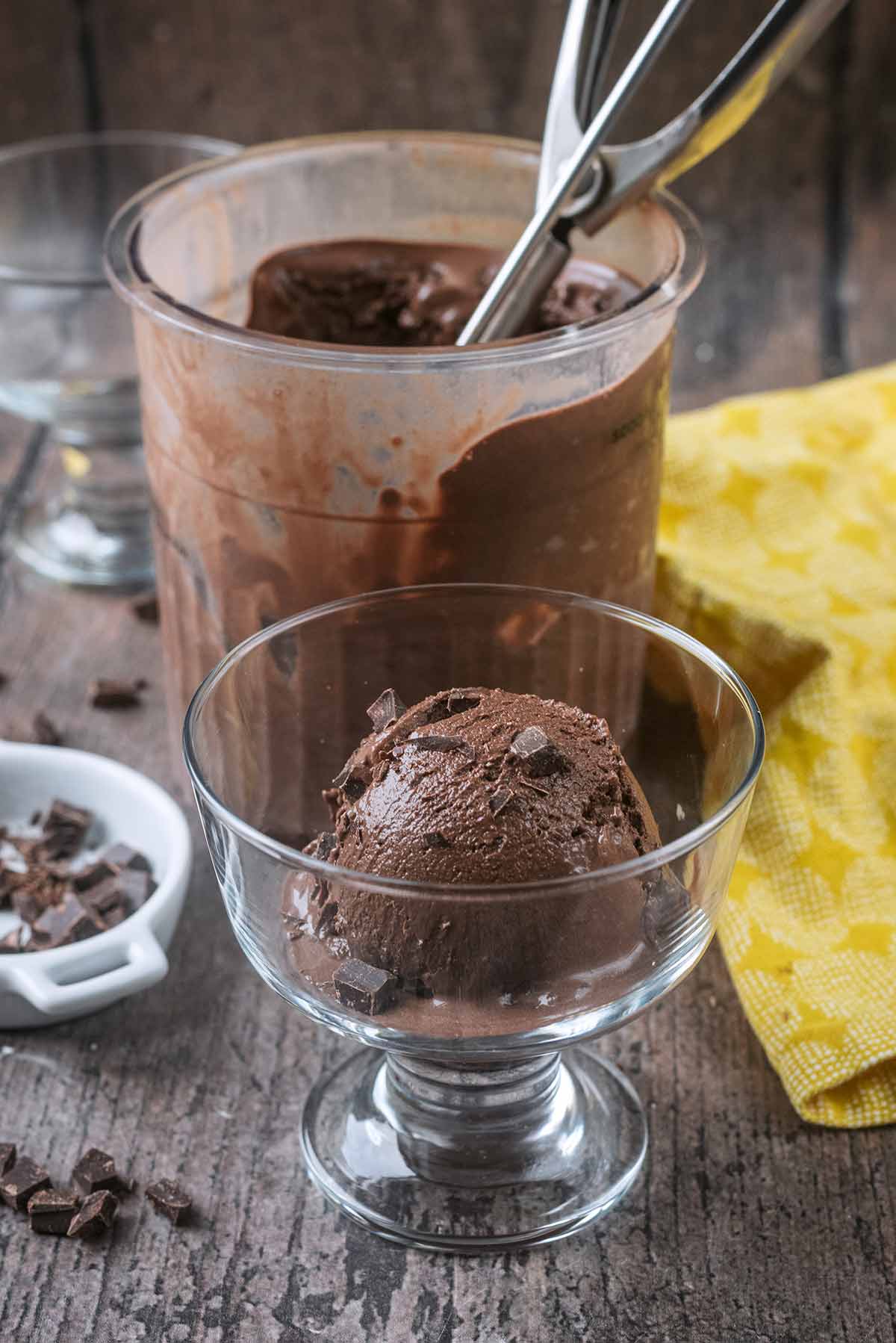 A ball of chocolate ice cream in a serving glass in front of a Ninja Creami tub.
