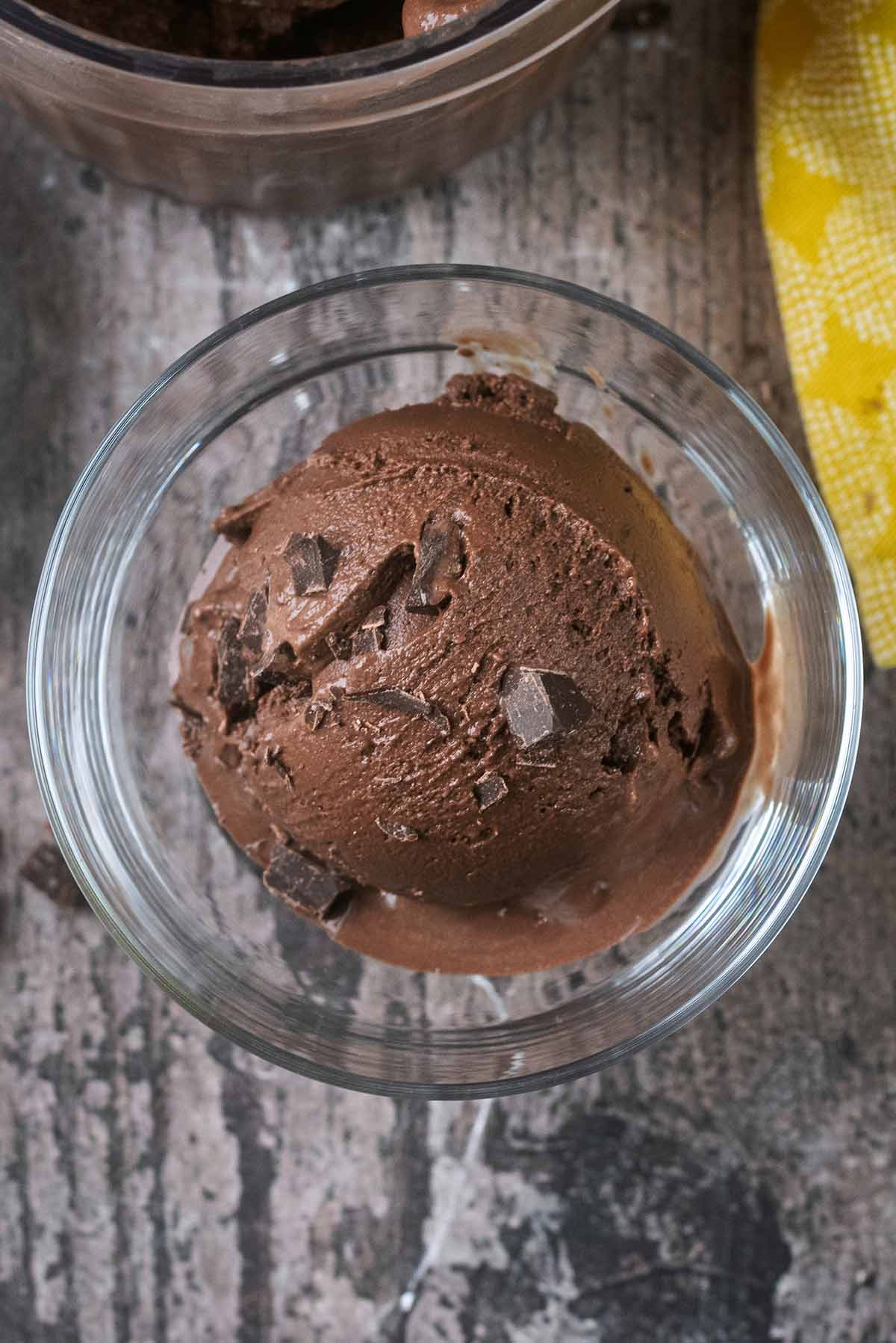 A ball of chocolate ice cream in a serving glass, topped with small chunks of chocolate.