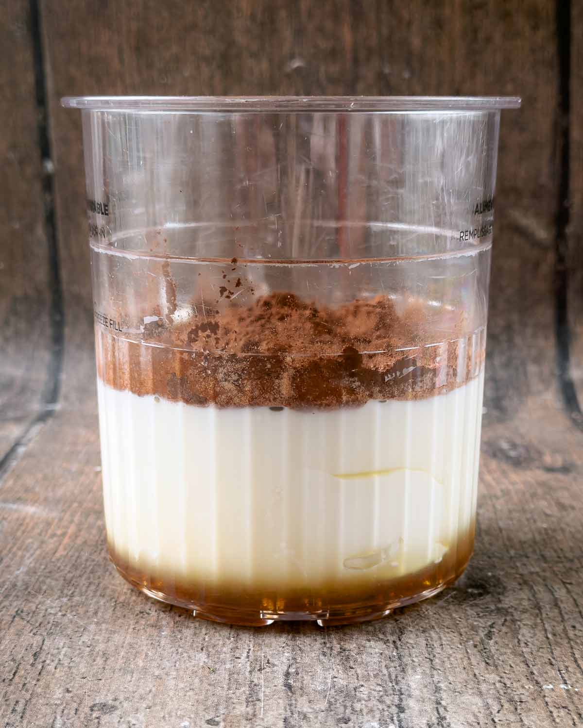A Ninja Creami tub containing yogurt, milk, maple syrup and cocoa powder.