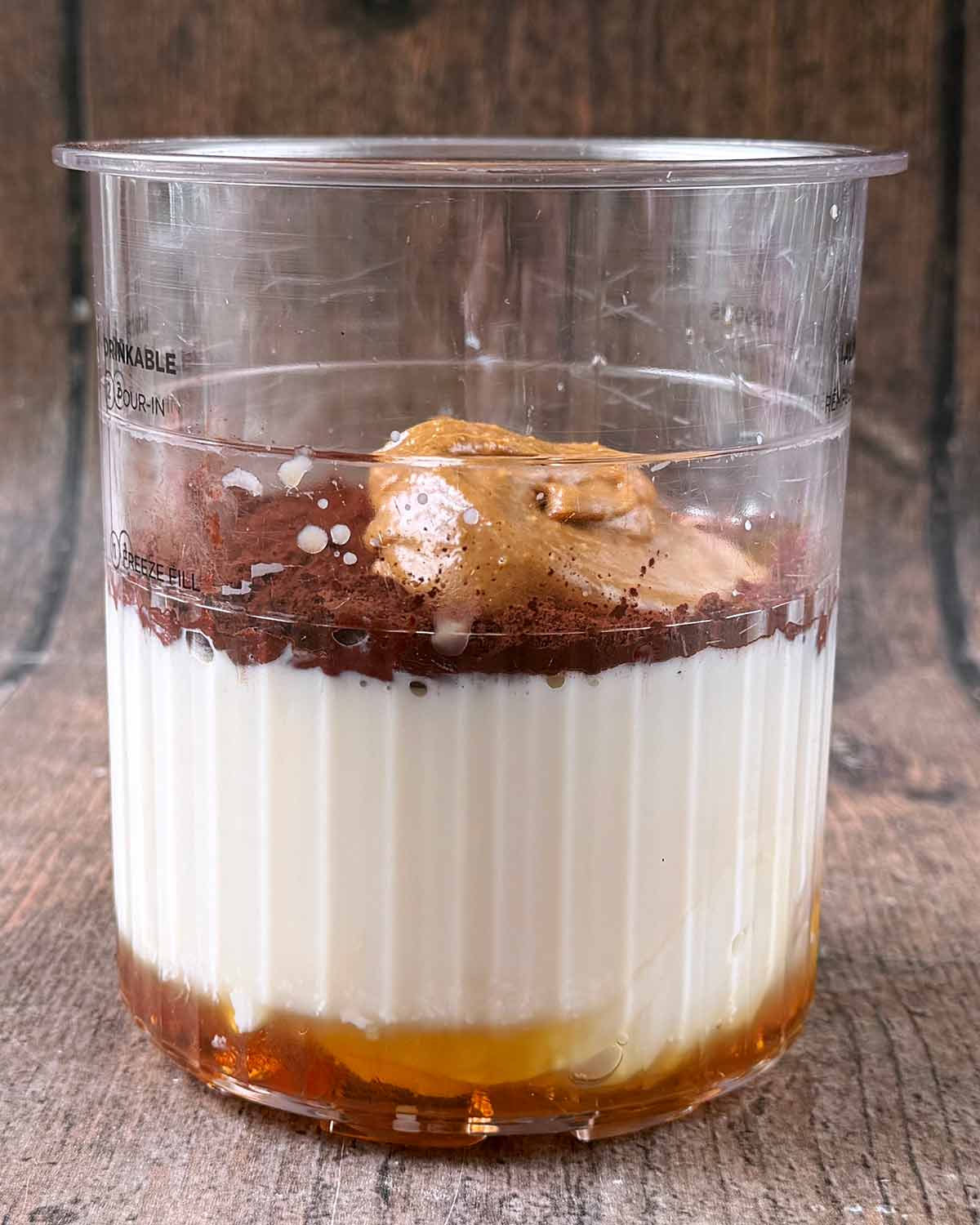 A Ninja Creami tub containing milk, yogurt, maple syrup, cocoa powder and peanut butter.