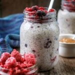A jar of overnight oats with frozen berries next to more frozen berries.