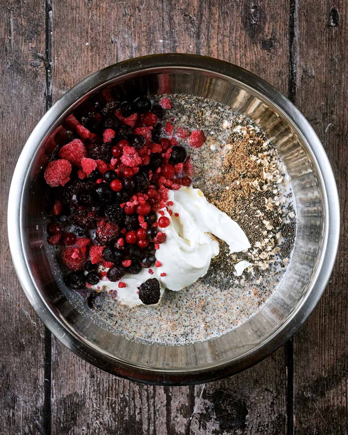 A mixing bowl containing oats, yogurt, milk, seeds and berries.