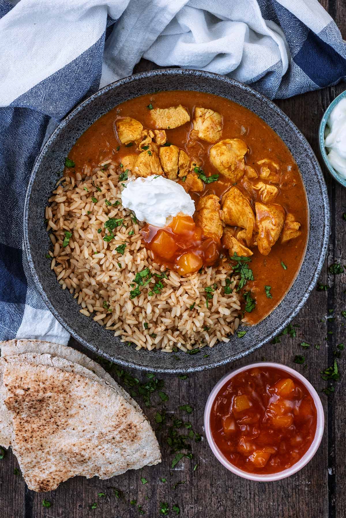 A bowl of curry and rice next to a small bowl of mango chutney and a folded flatbread.